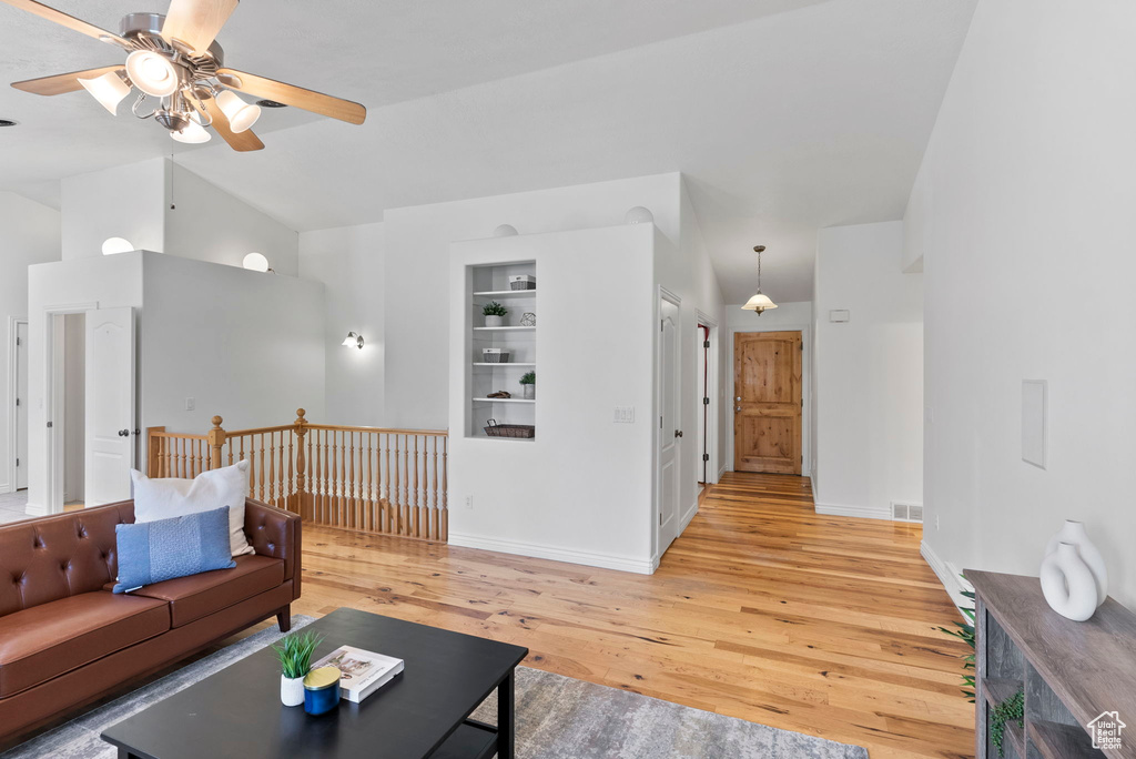 Living room with built in features, light hardwood / wood-style flooring, high vaulted ceiling, and ceiling fan