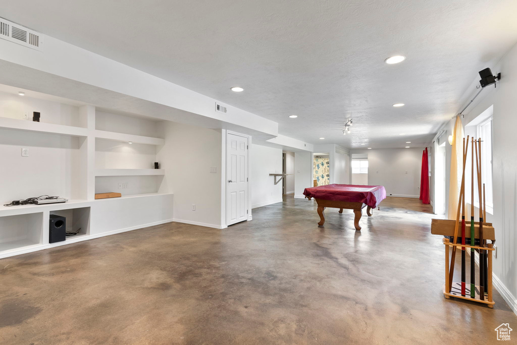 Recreation room featuring concrete floors, a textured ceiling, built in shelves, and billiards