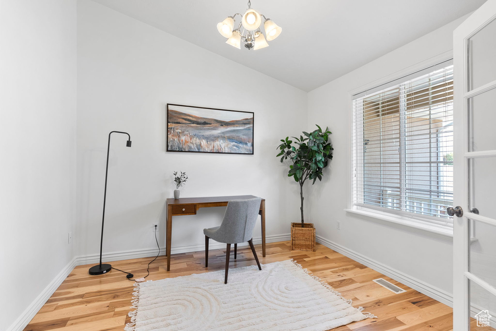 Home office with light hardwood / wood-style floors, vaulted ceiling, and a notable chandelier