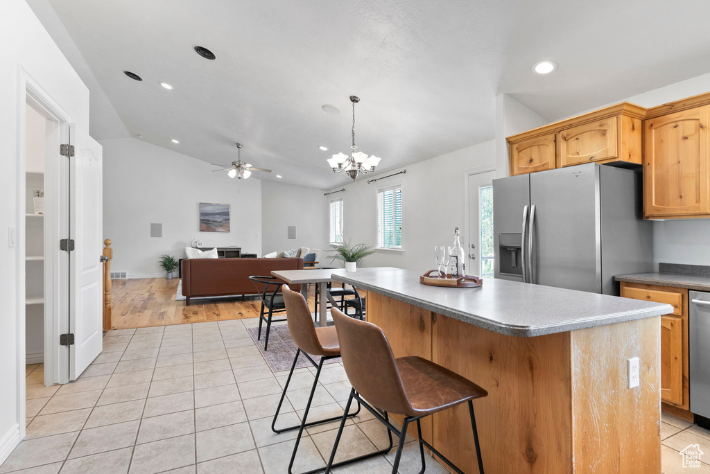 Kitchen with ceiling fan with notable chandelier, pendant lighting, a center island, appliances with stainless steel finishes, and light hardwood / wood-style flooring