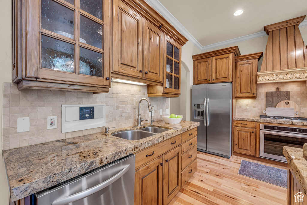 Kitchen with stainless steel appliances, premium range hood, backsplash, light wood-type flooring, and ornamental molding