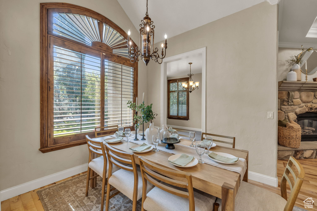 Dining room with wood-type flooring, a fireplace, vaulted ceiling, and a chandelier