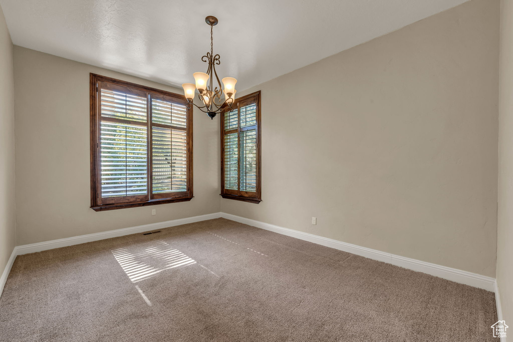 Carpeted spare room featuring a chandelier