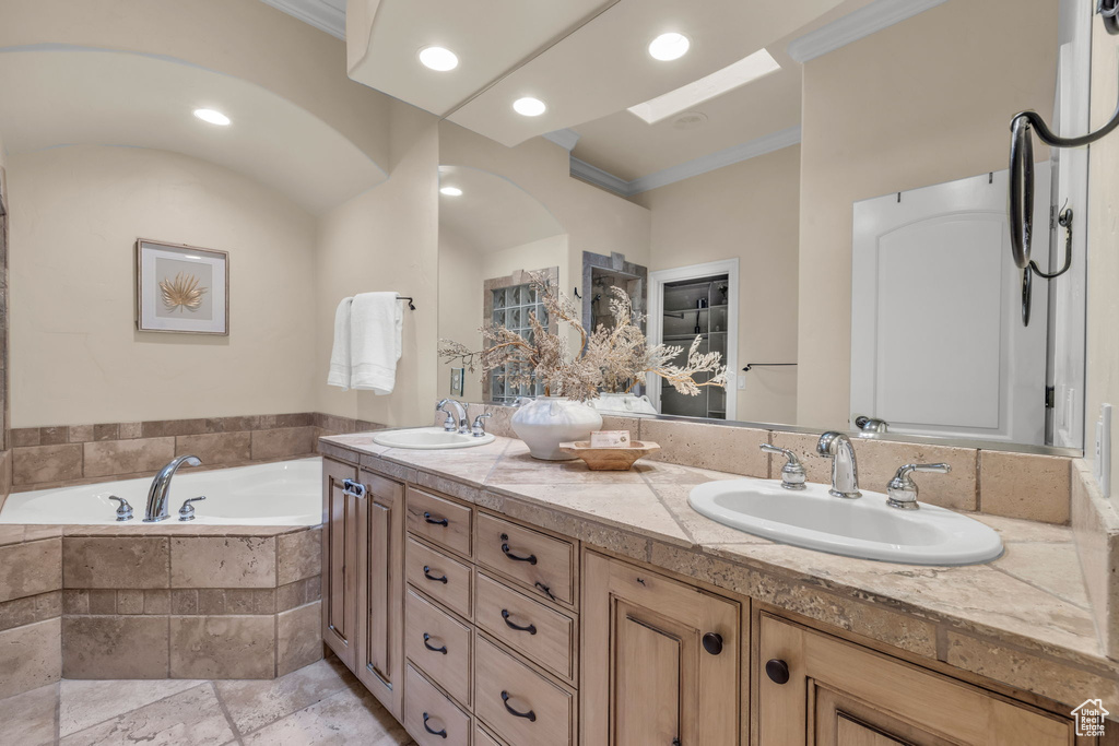 Bathroom with tile patterned floors, tiled tub, ornamental molding, and dual bowl vanity