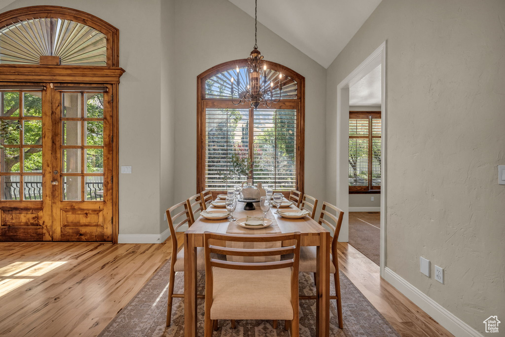 Dining room featuring hardwood / wood-style flooring, vaulted ceiling, french doors, and a notable chandelier