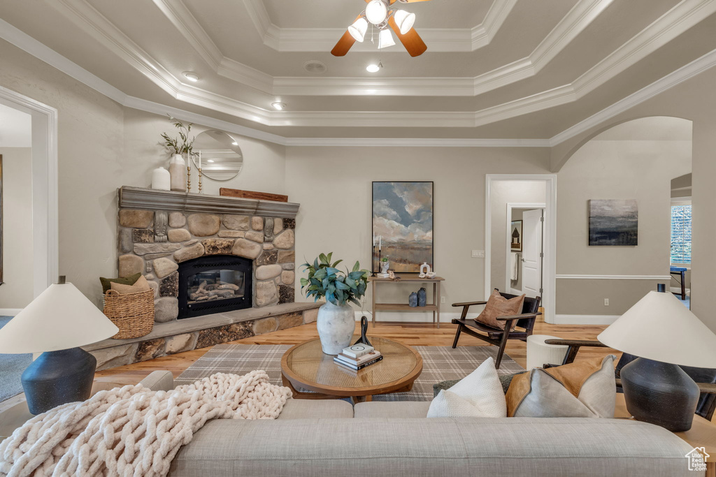 Living room featuring crown molding, a fireplace, ceiling fan, and a raised ceiling