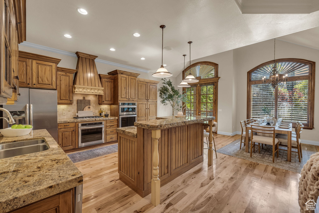 Kitchen featuring tasteful backsplash, stainless steel appliances, a breakfast bar area, custom range hood, and light hardwood / wood-style floors