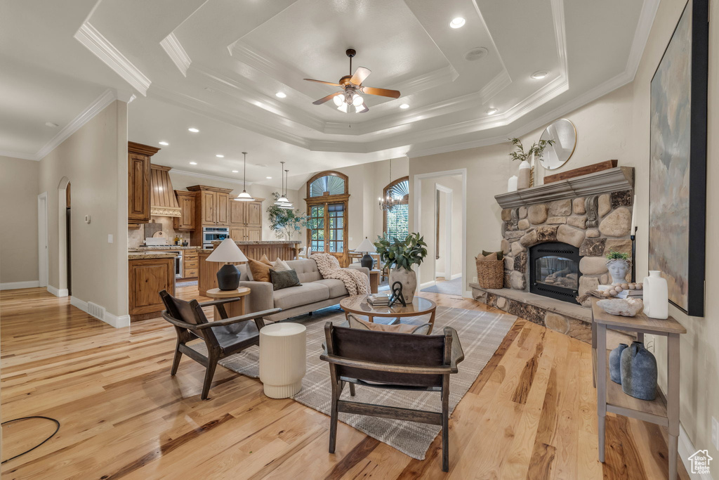 Living room featuring a fireplace, a tray ceiling, light wood-type flooring, and ceiling fan