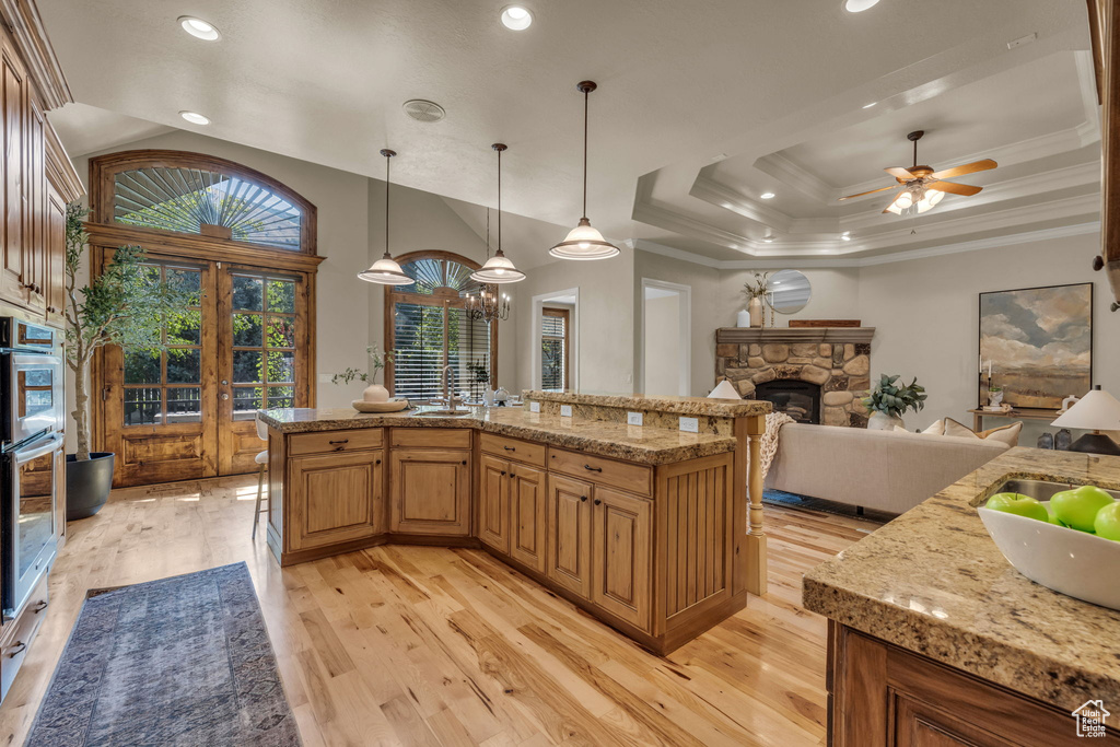 Kitchen with light hardwood / wood-style flooring, a fireplace, pendant lighting, light stone counters, and ceiling fan