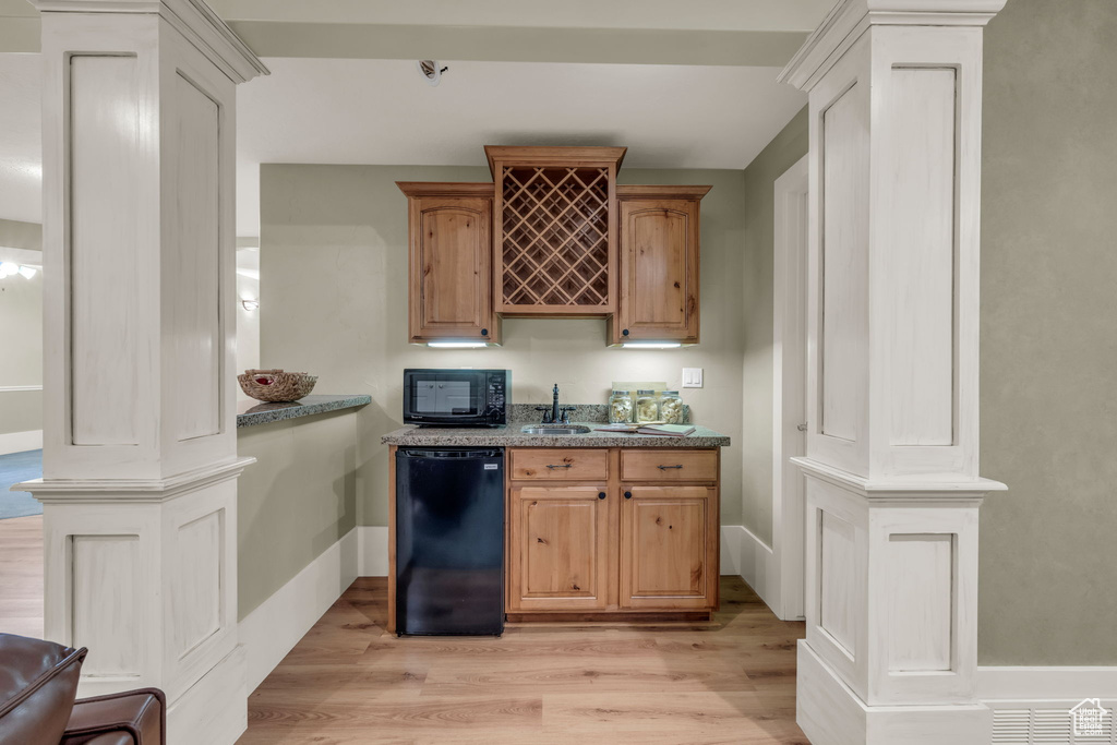 Kitchen featuring black appliances, sink, light hardwood / wood-style floors, ornate columns, and stone countertops