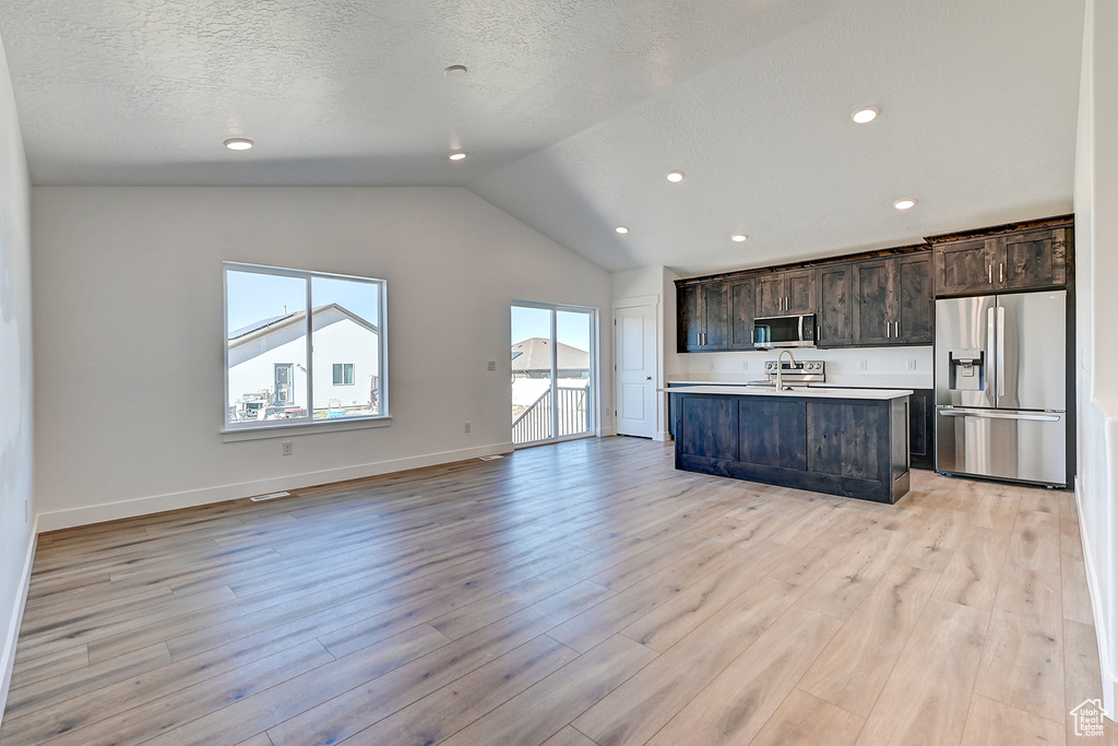 Kitchen featuring a center island with sink, dark brown cabinetry, appliances with stainless steel finishes, and light wood-type flooring