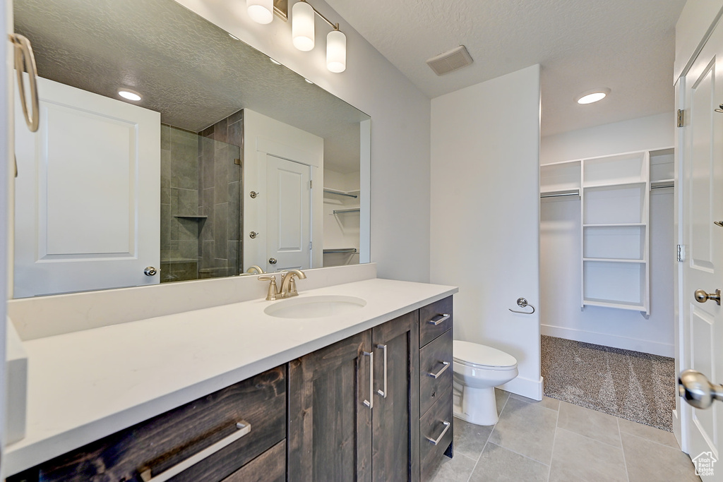 Bathroom featuring tiled shower, vanity, tile patterned flooring, and toilet