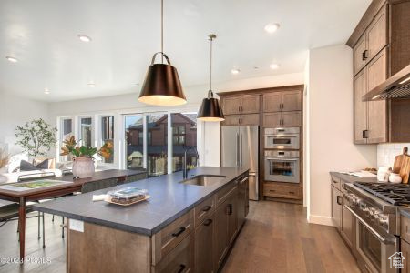 Kitchen featuring wall chimney range hood, a kitchen island with sink, appliances with stainless steel finishes, hardwood / wood-style flooring, and sink