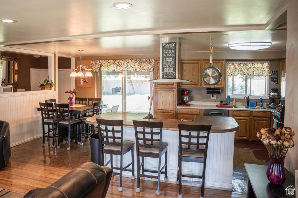 Kitchen with wall chimney range hood, stainless steel dishwasher, sink, and wood-type flooring