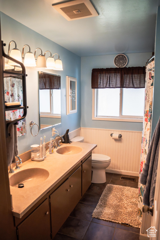 Bathroom with a healthy amount of sunlight, tile patterned floors, toilet, and dual bowl vanity