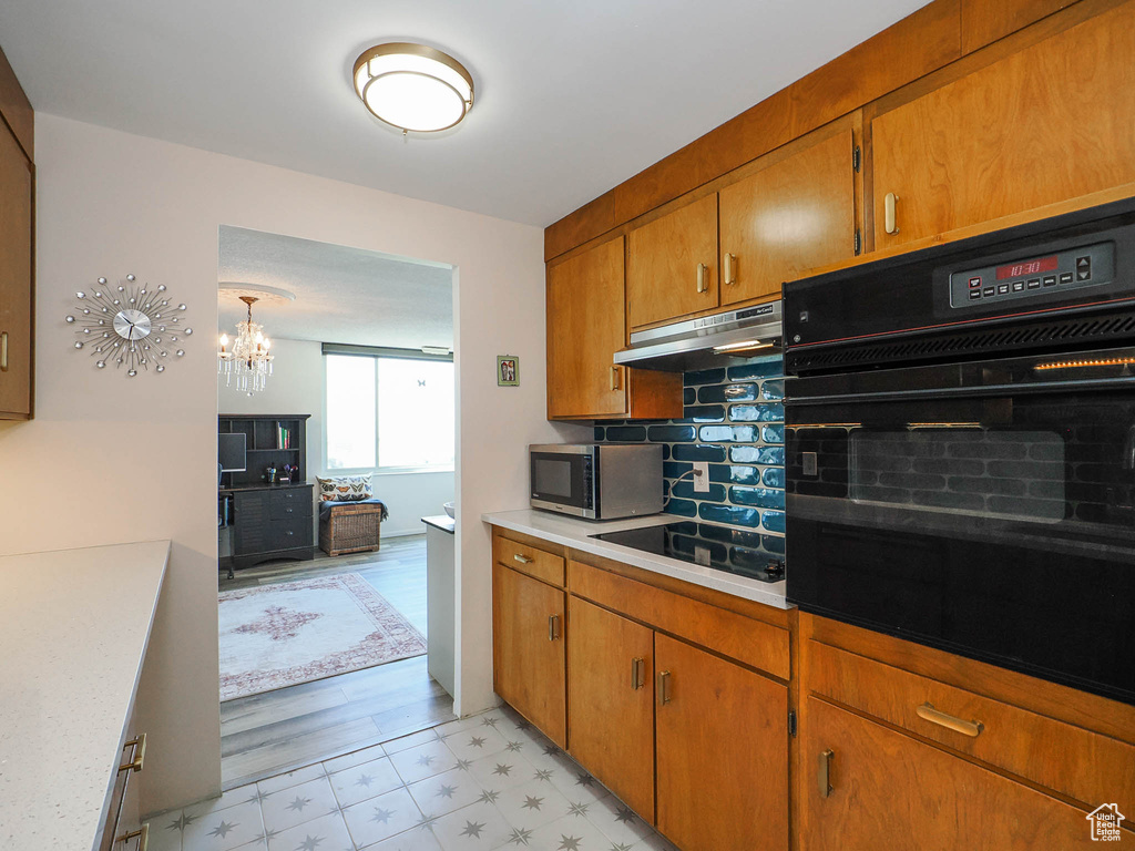 Kitchen with a chandelier, light hardwood / wood-style floors, black appliances, decorative backsplash, and pendant lighting