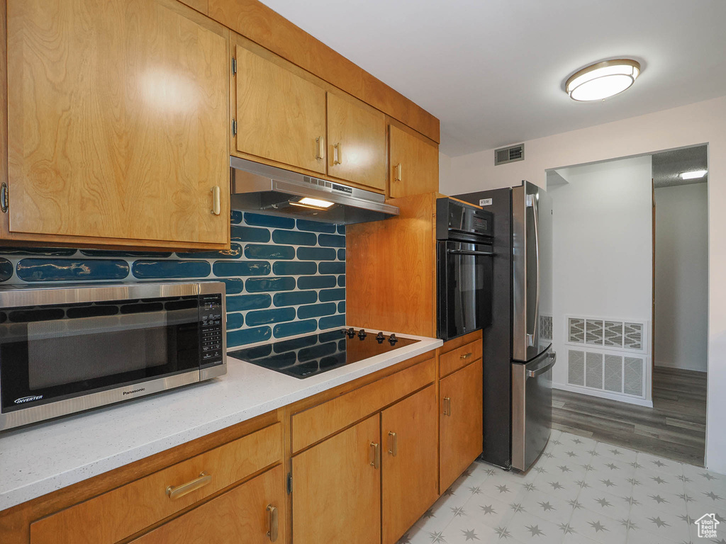 Kitchen with backsplash, black appliances, and light hardwood / wood-style flooring