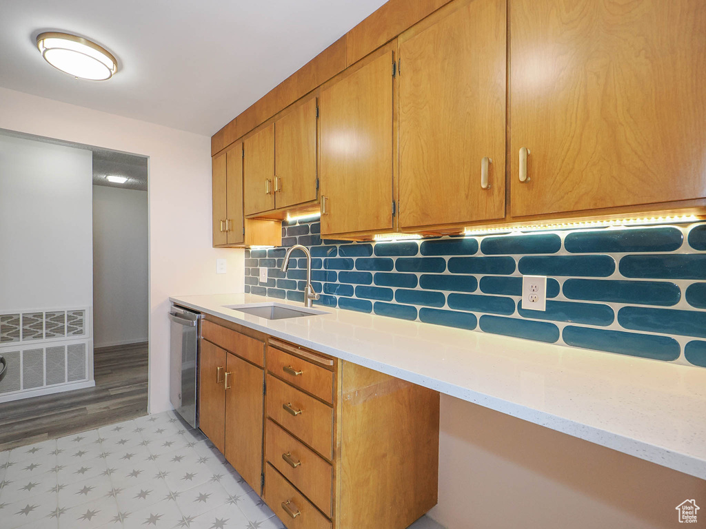 Kitchen featuring stainless steel dishwasher, sink, backsplash, and light wood-type flooring