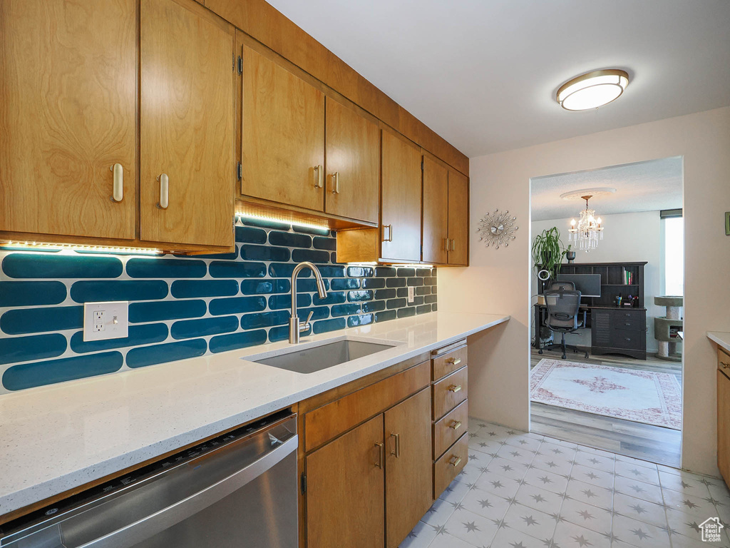 Kitchen with a notable chandelier, stainless steel dishwasher, light wood-type flooring, sink, and backsplash