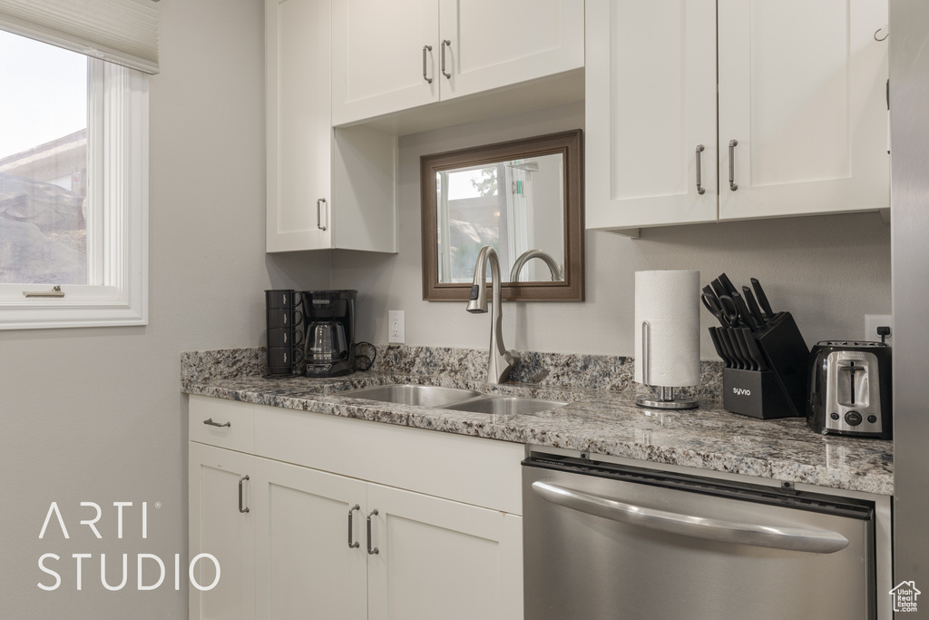 Kitchen featuring white cabinetry, dishwasher, light stone countertops, and sink