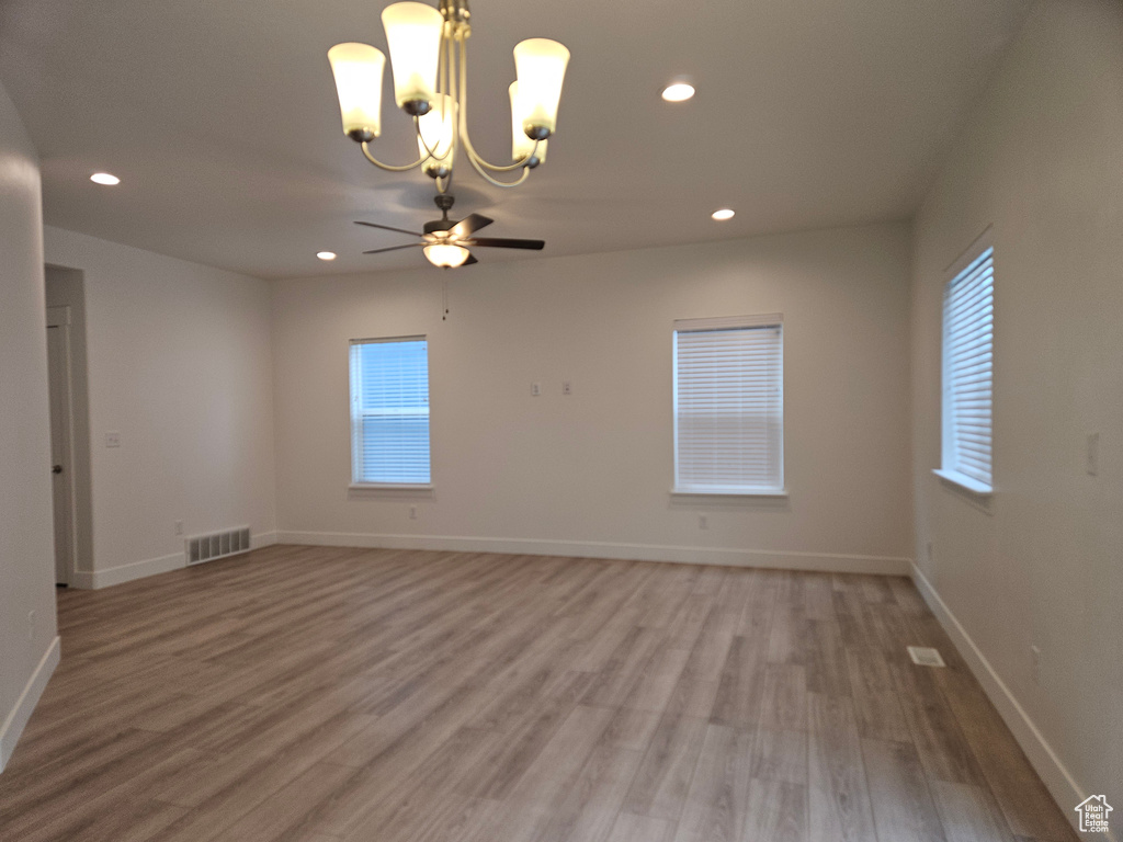 Empty room featuring ceiling fan with notable chandelier and hardwood / wood-style floors