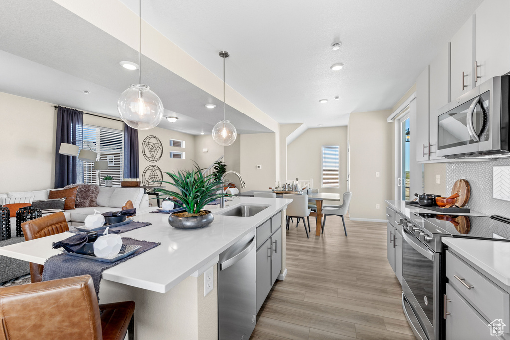 Kitchen featuring decorative light fixtures, an island with sink, light hardwood / wood-style floors, appliances with stainless steel finishes, and backsplash