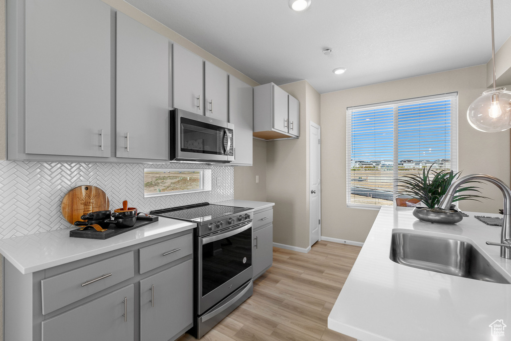 Kitchen with light hardwood / wood-style flooring, stainless steel appliances, decorative backsplash, pendant lighting, and sink