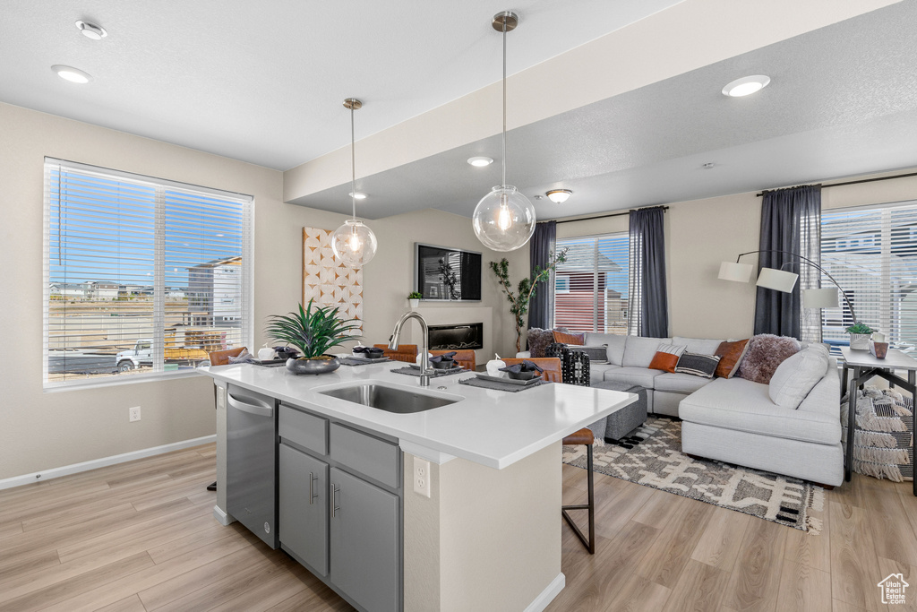 Kitchen with a center island with sink, sink, pendant lighting, dishwashing machine, and light wood-type flooring