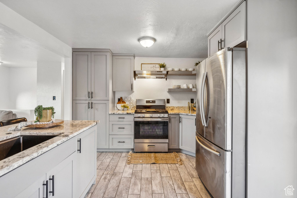 Kitchen featuring stainless steel appliances, wall chimney exhaust hood, light stone countertops, light hardwood / wood-style flooring, and gray cabinetry