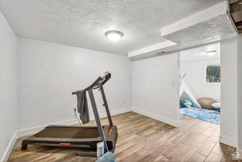 Workout area with a textured ceiling and light hardwood / wood-style floors