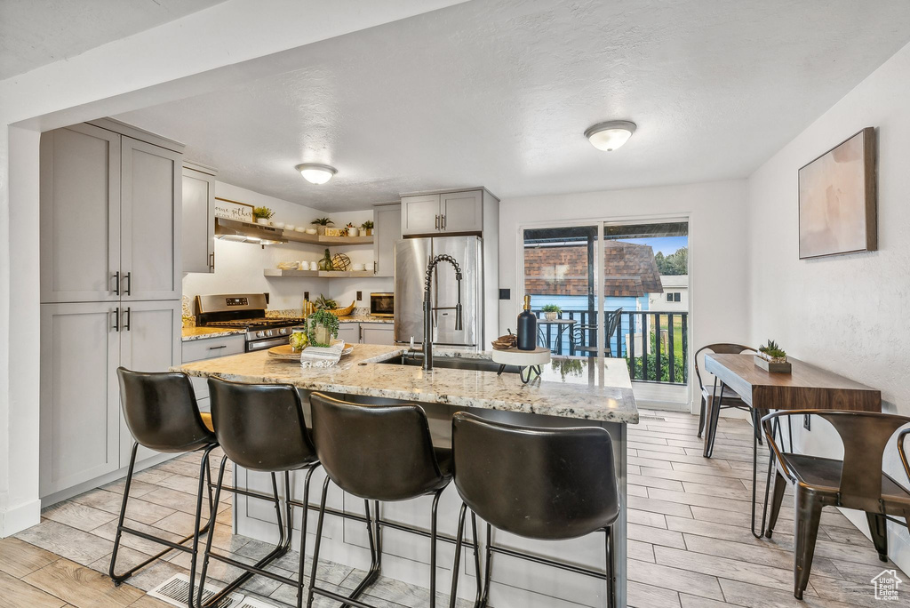 Kitchen with a center island with sink, light wood-type flooring, stainless steel appliances, and gray cabinets