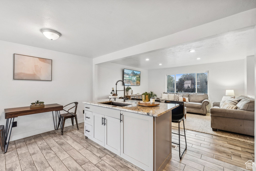 Kitchen with sink, light hardwood / wood-style flooring, a breakfast bar area, and an island with sink