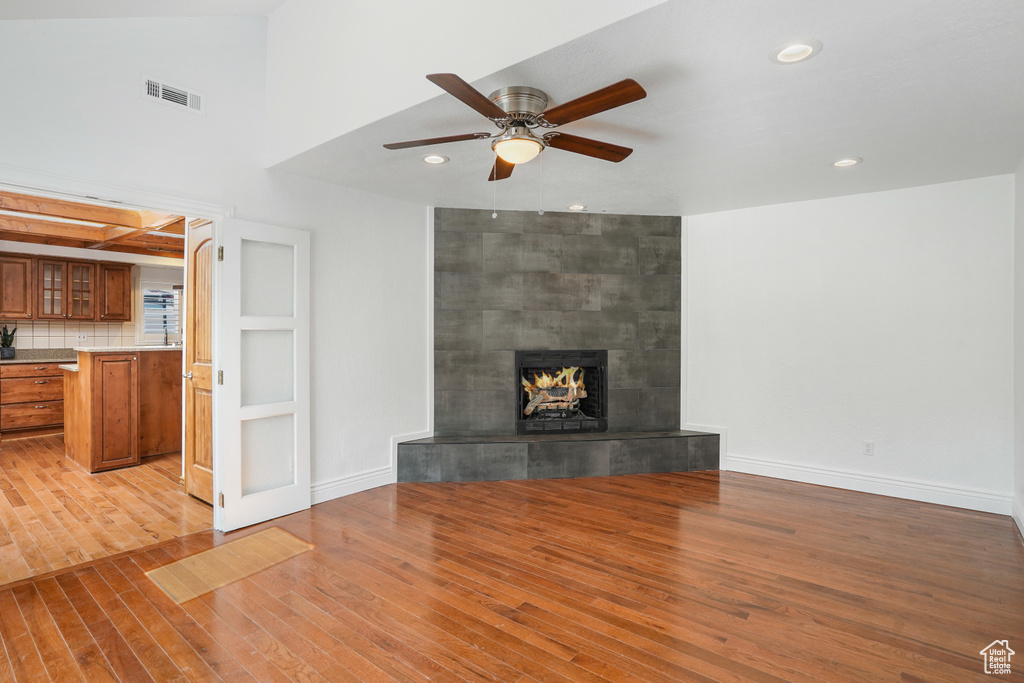 Unfurnished living room with a tile fireplace, ceiling fan, and light wood-type flooring