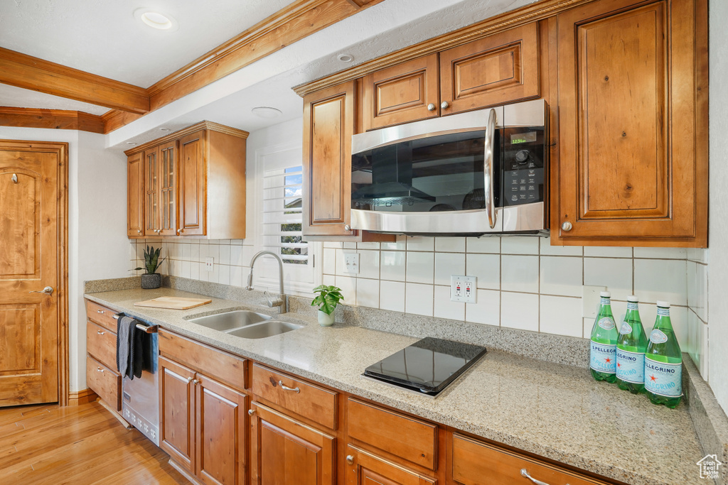 Kitchen featuring black electric cooktop, tasteful backsplash, light wood-type flooring, dishwasher, and sink