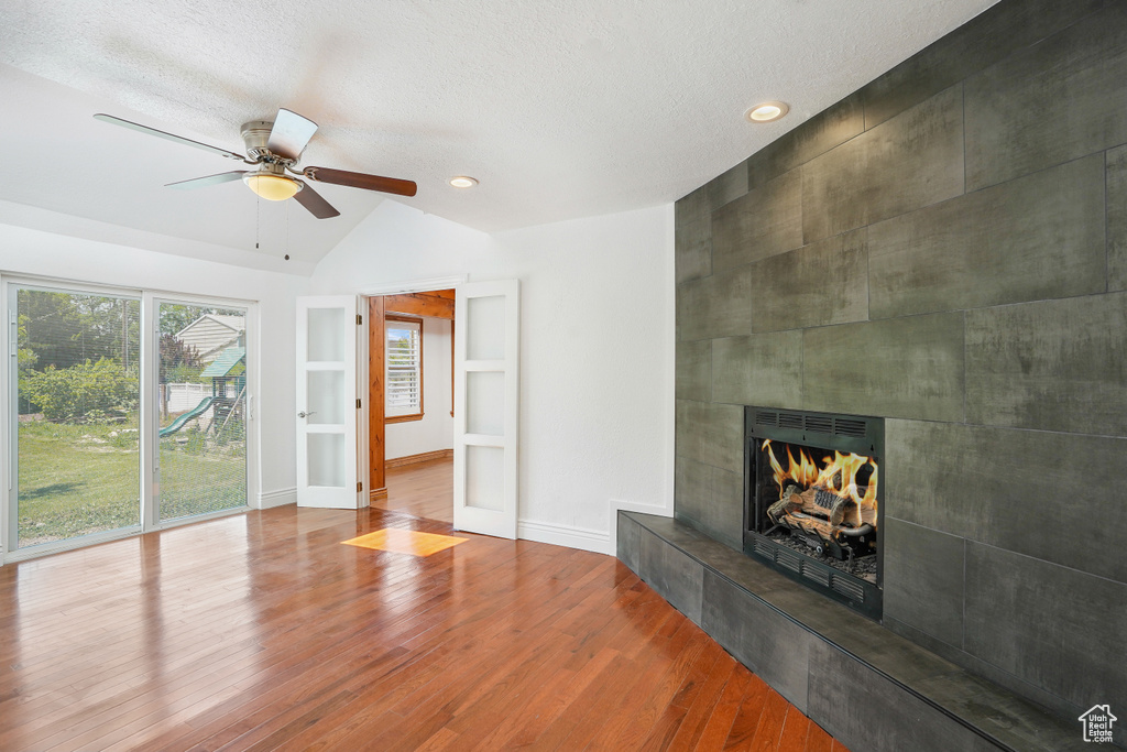 Unfurnished living room featuring built in features, hardwood / wood-style flooring, a fireplace, lofted ceiling, and ceiling fan