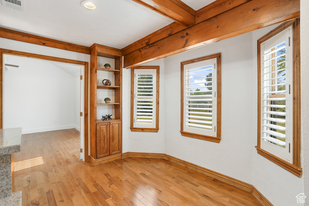 Spare room featuring beam ceiling, light hardwood / wood-style flooring, and a healthy amount of sunlight