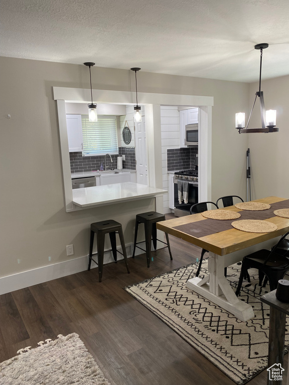 Dining space with sink, a textured ceiling, a chandelier, and dark wood-type flooring