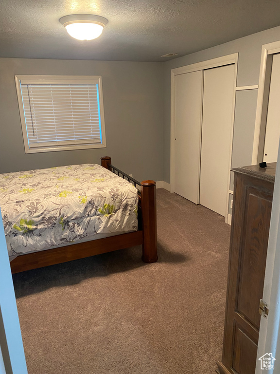 Bedroom with a closet, a textured ceiling, and dark carpet