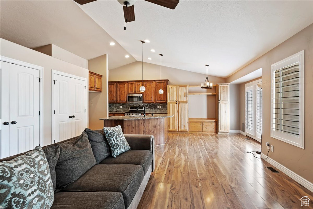 Living room with vaulted ceiling, ceiling fan with notable chandelier, and light wood-type flooring