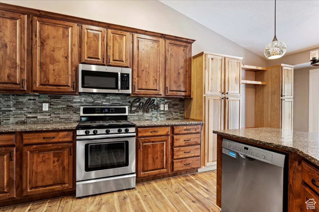 Kitchen with appliances with stainless steel finishes, stone counters, vaulted ceiling, backsplash, and light wood-type flooring