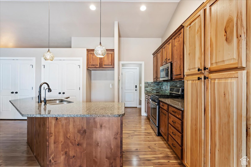 Kitchen with light hardwood / wood-style flooring, stainless steel appliances, light stone countertops, decorative light fixtures, and sink