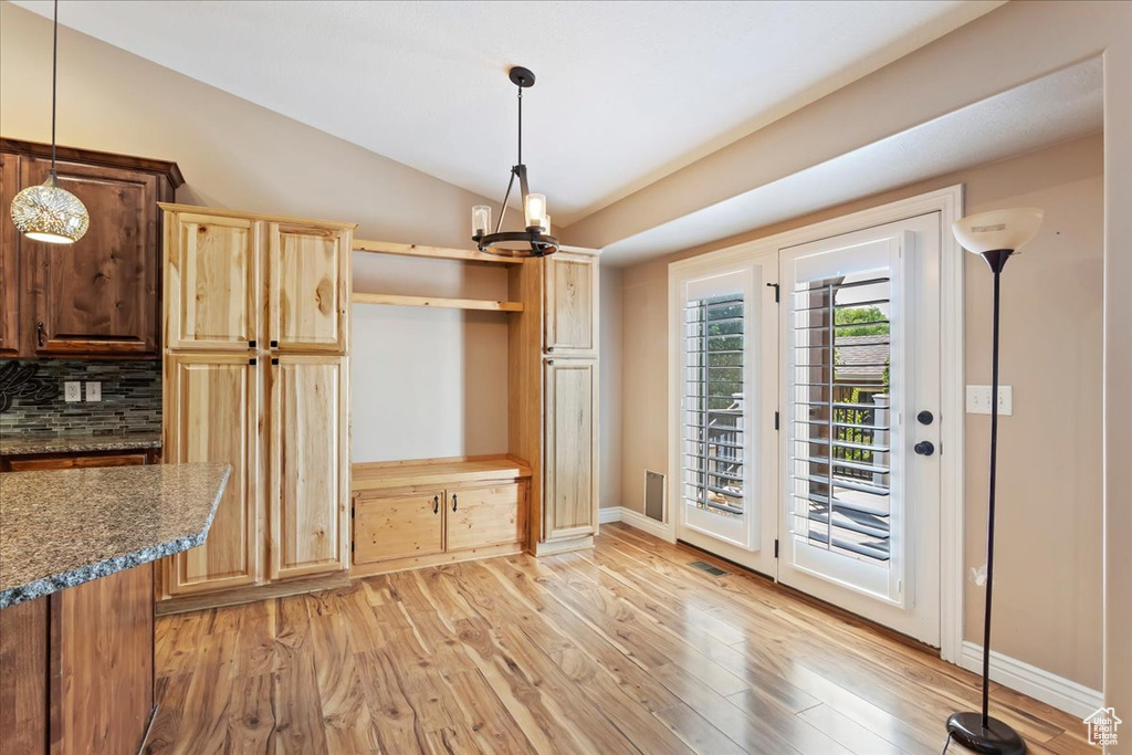 Kitchen with hanging light fixtures, decorative backsplash, an inviting chandelier, light hardwood / wood-style floors, and lofted ceiling