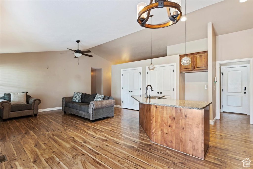 Kitchen with hardwood / wood-style floors, sink, pendant lighting, light stone countertops, and ceiling fan