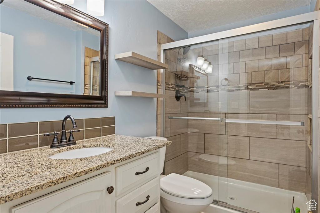 Bathroom with a shower with door, tasteful backsplash, a textured ceiling, toilet, and vanity