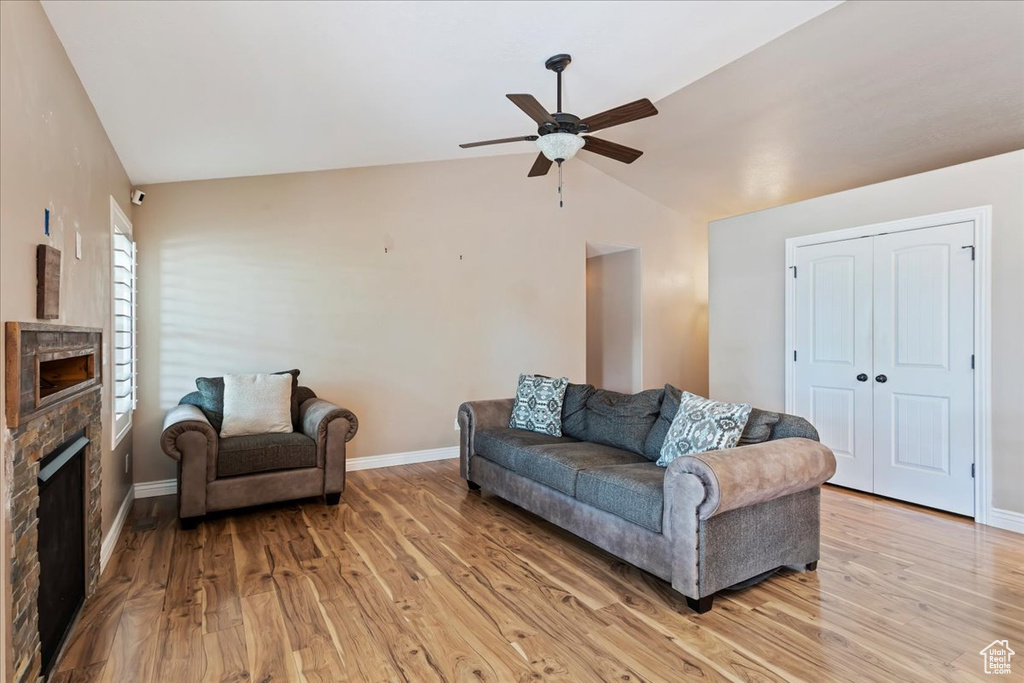 Living room featuring a stone fireplace, ceiling fan, light hardwood / wood-style flooring, and high vaulted ceiling