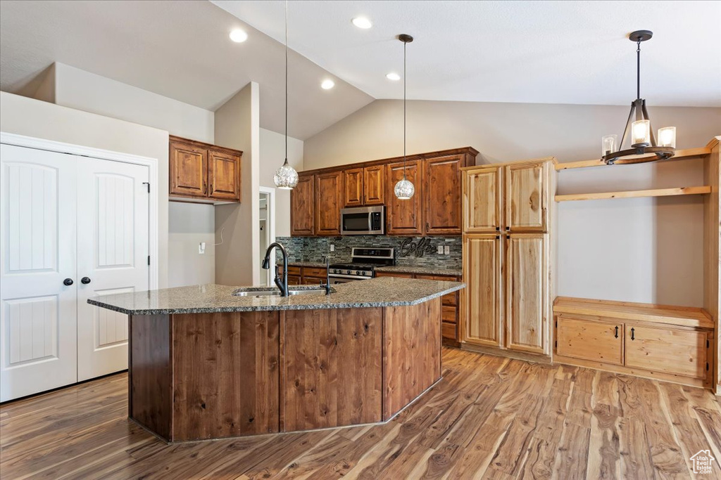 Kitchen featuring appliances with stainless steel finishes, a center island with sink, hardwood / wood-style floors, sink, and lofted ceiling