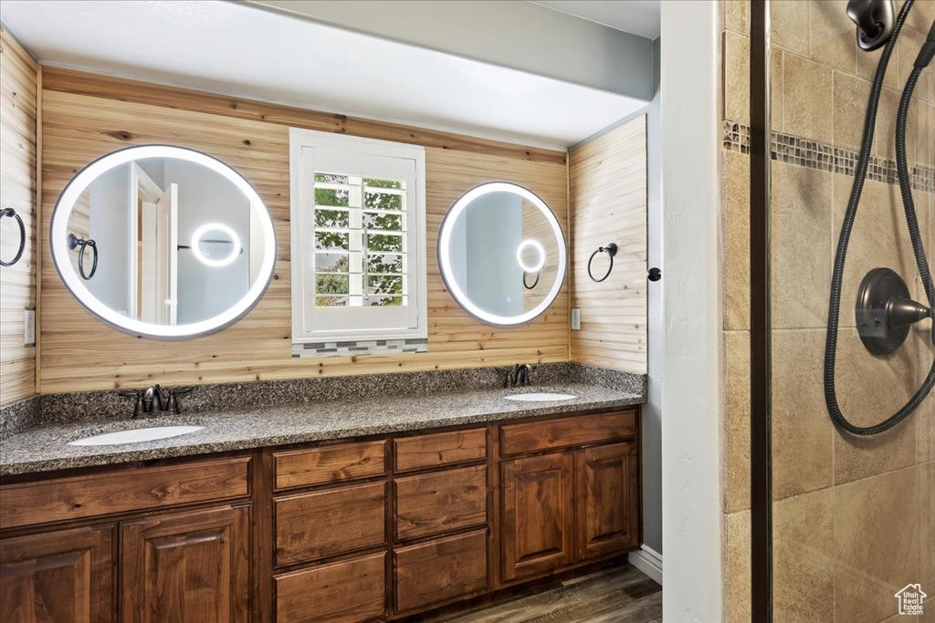 Bathroom featuring double vanity, wood walls, hardwood / wood-style floors, and a shower