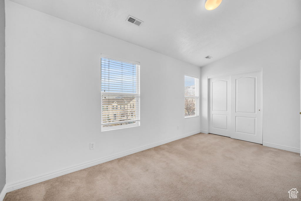 Unfurnished bedroom featuring a closet, lofted ceiling, and light colored carpet