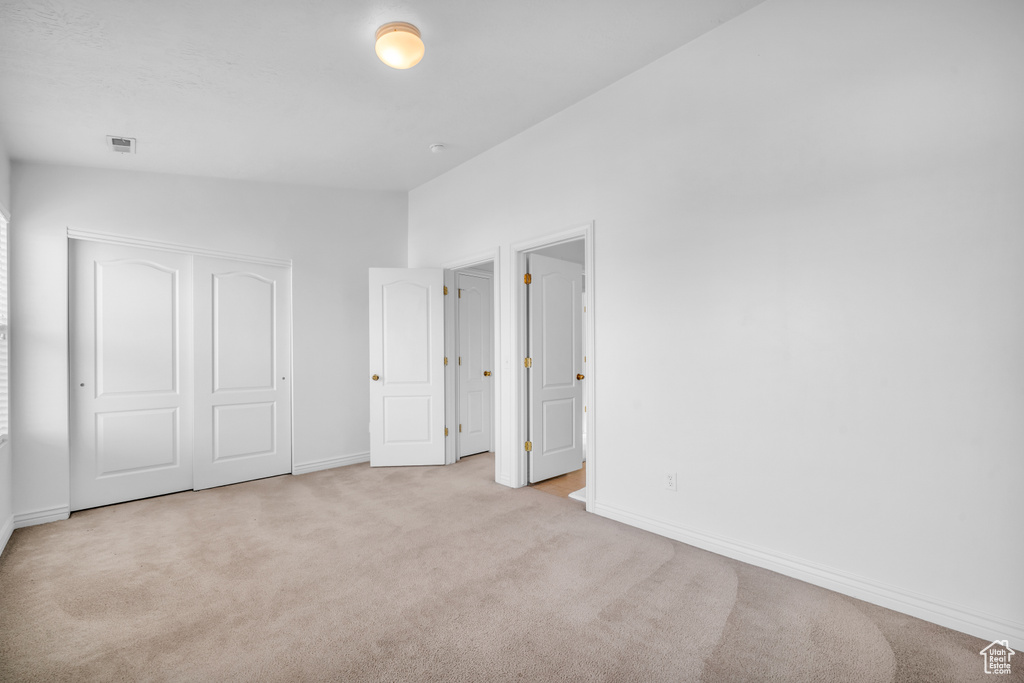 Unfurnished bedroom featuring light carpet, a closet, and vaulted ceiling