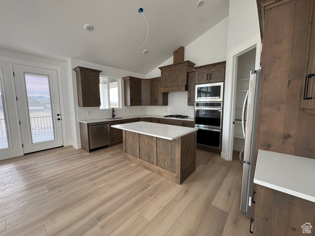 Kitchen with appliances with stainless steel finishes, tasteful backsplash, vaulted ceiling, sink, and a center island